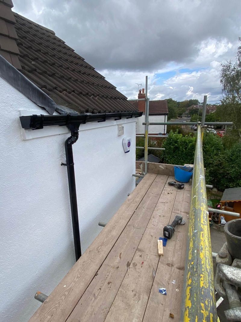 New black gutter and downpipe on the corner of a white rendered wall