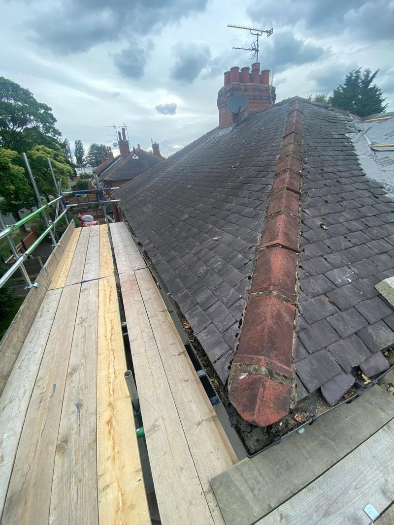 The old grey roof covering and ridge before the work, with the chimney and neighbouring rooftops behind