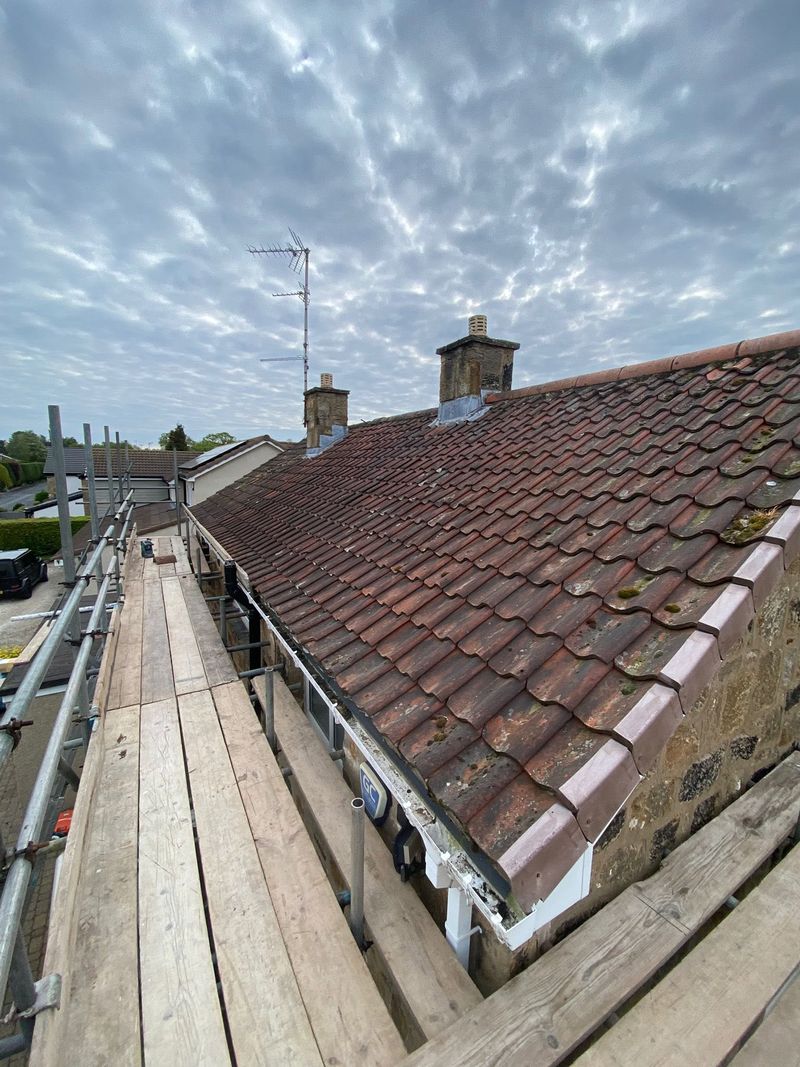 Old weathered red roof tiles on a house, seen from the scaffold before the work